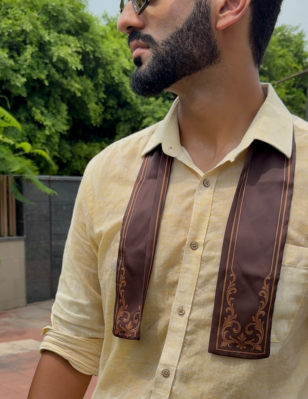 Man wearing a beige shirt with brown decorative scarf outdoors