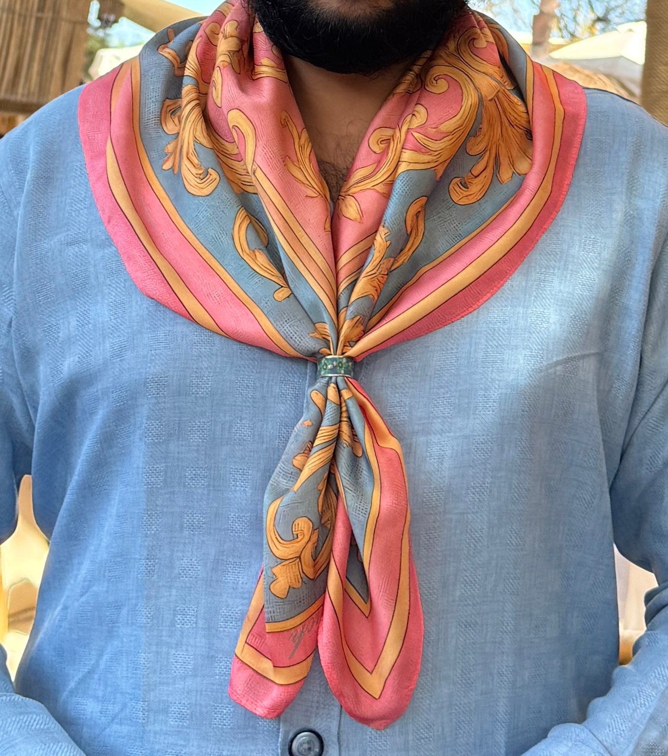 Person wearing a patterned scarf on a blue shirt outdoors