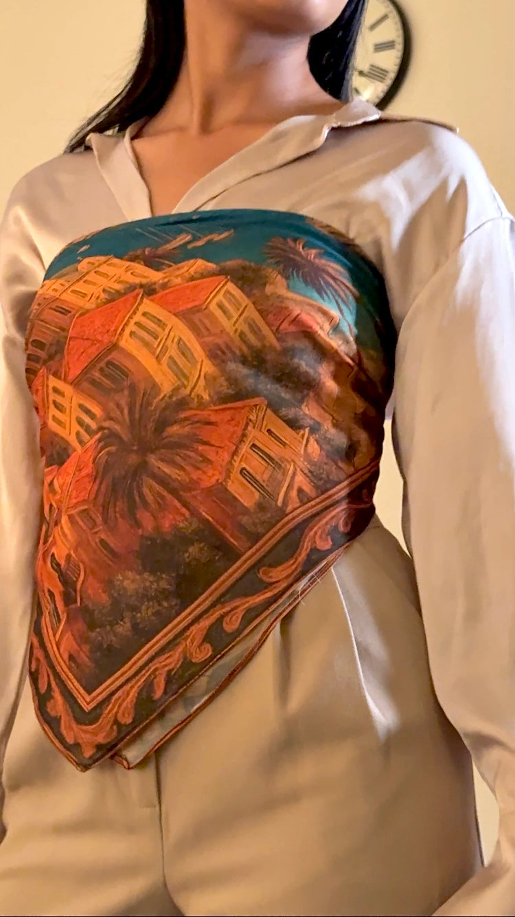 Person wearing a decorative scarf with a scenic design on a plain background