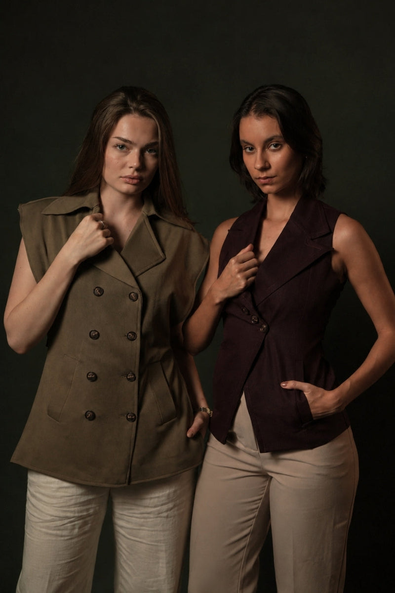 Two women side by side, one in an olive sleeveless double-breasted blazer and one in a plum single-breasted waistcoat, both over cream trousers