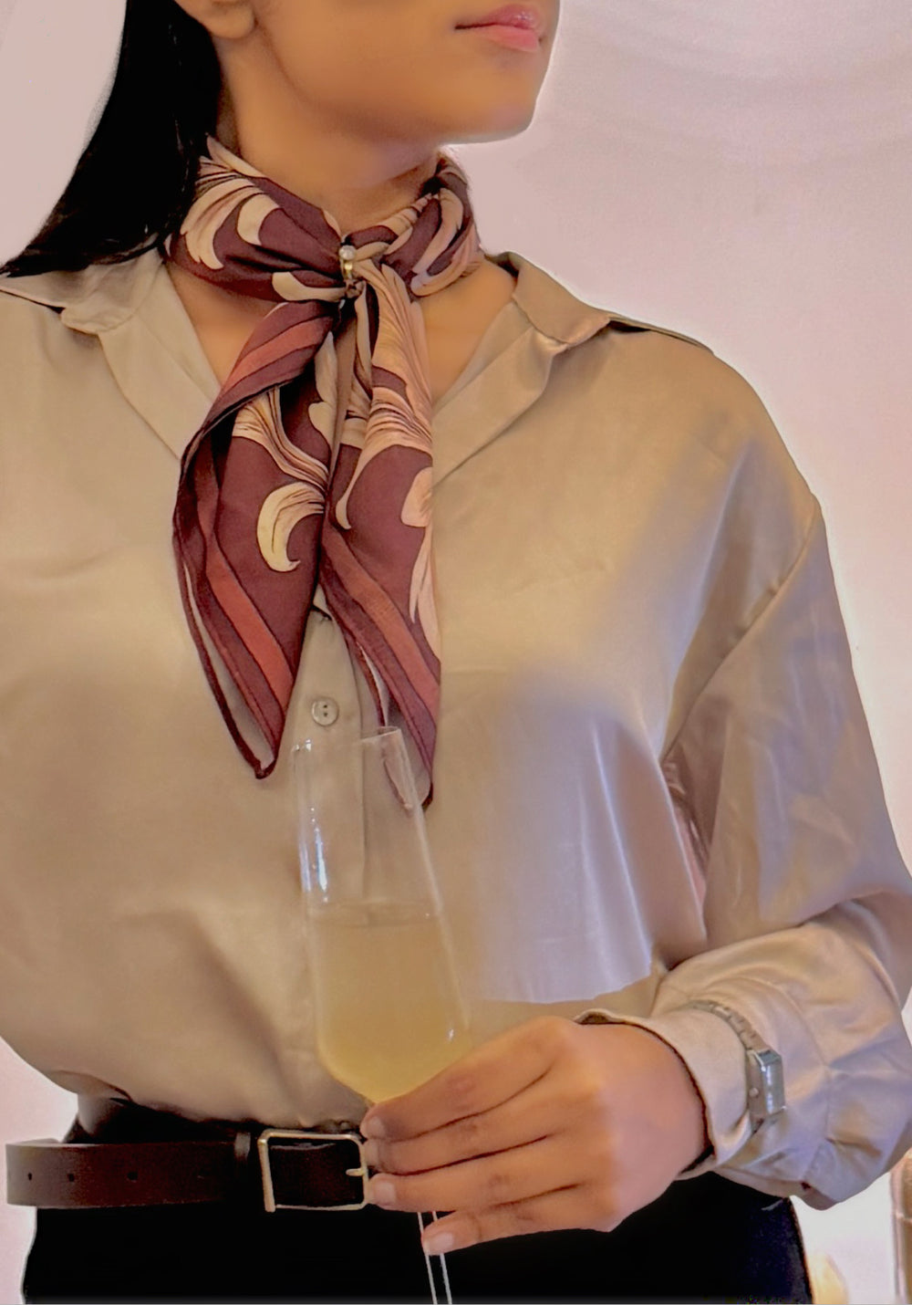 Person wearing a patterned scarf and holding a glass with a light-colored beverage.