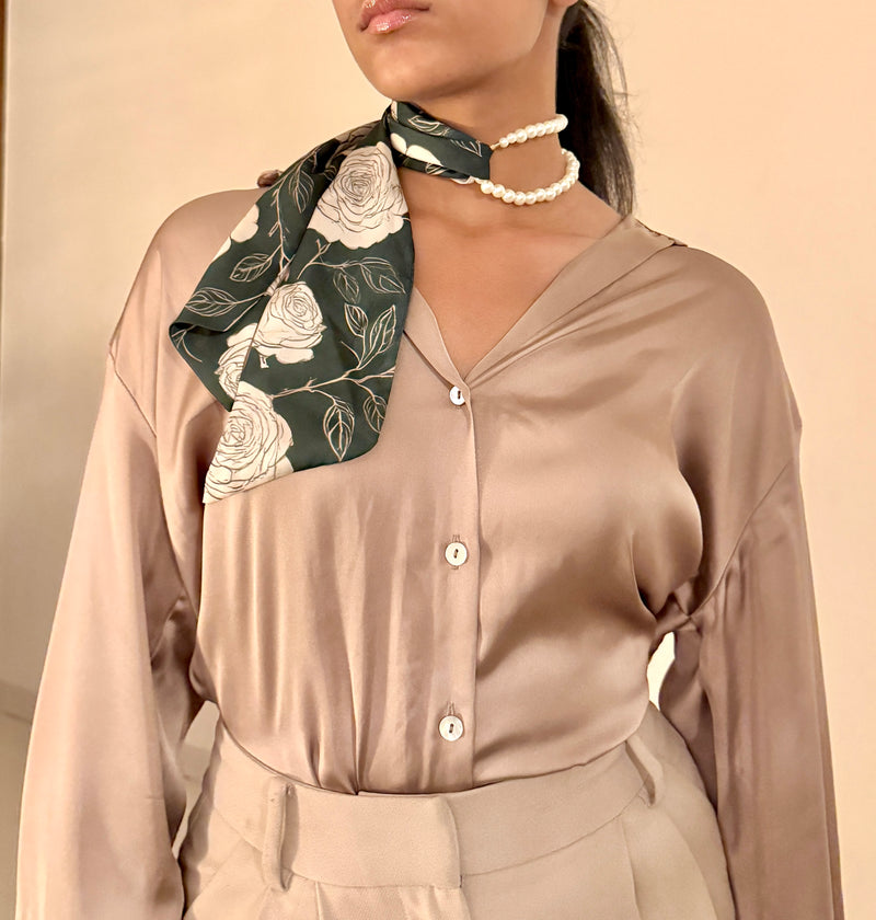 Woman wearing a beige shirt with a floral scarf around her neck against a beige background