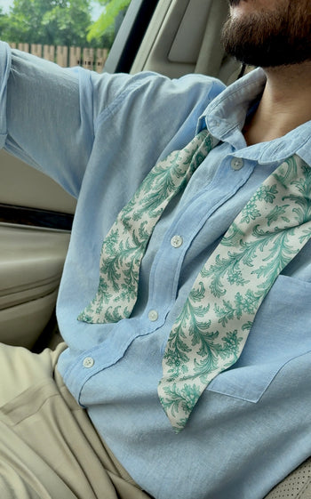Person wearing a light blue shirt with a green patterned scarf inside a vehicle.