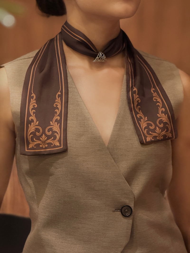 Person wearing a brown vest with decorative elements and a matching scarf.