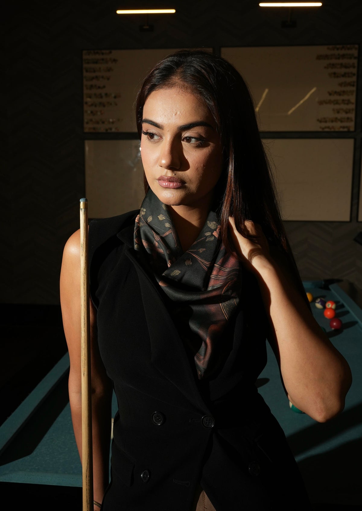 Woman adjusting a patterned scarf in a dimly lit room