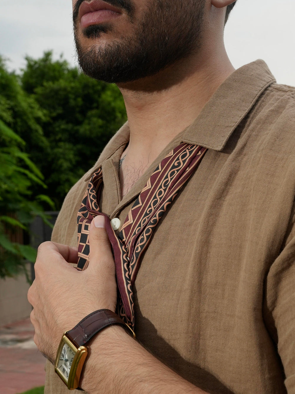Man wearing a scarf with intricate patterns, outdoors.