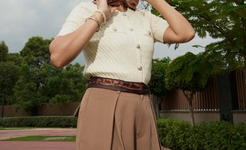 Person wearing a cream sweater and beige pants with a printed scarf as belt, standing outdoors.